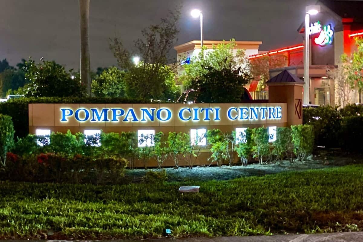 Een bord voor Pompano Citi Centre met een goed verlichte ingang en omliggend groen.