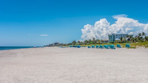Ein Strand mit einem Hotel im Hintergrund, klarem Himmel und einer großen Wolkenformation.