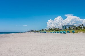 A beach with a hotel in the background, a clear sky, and a large cloud formation.