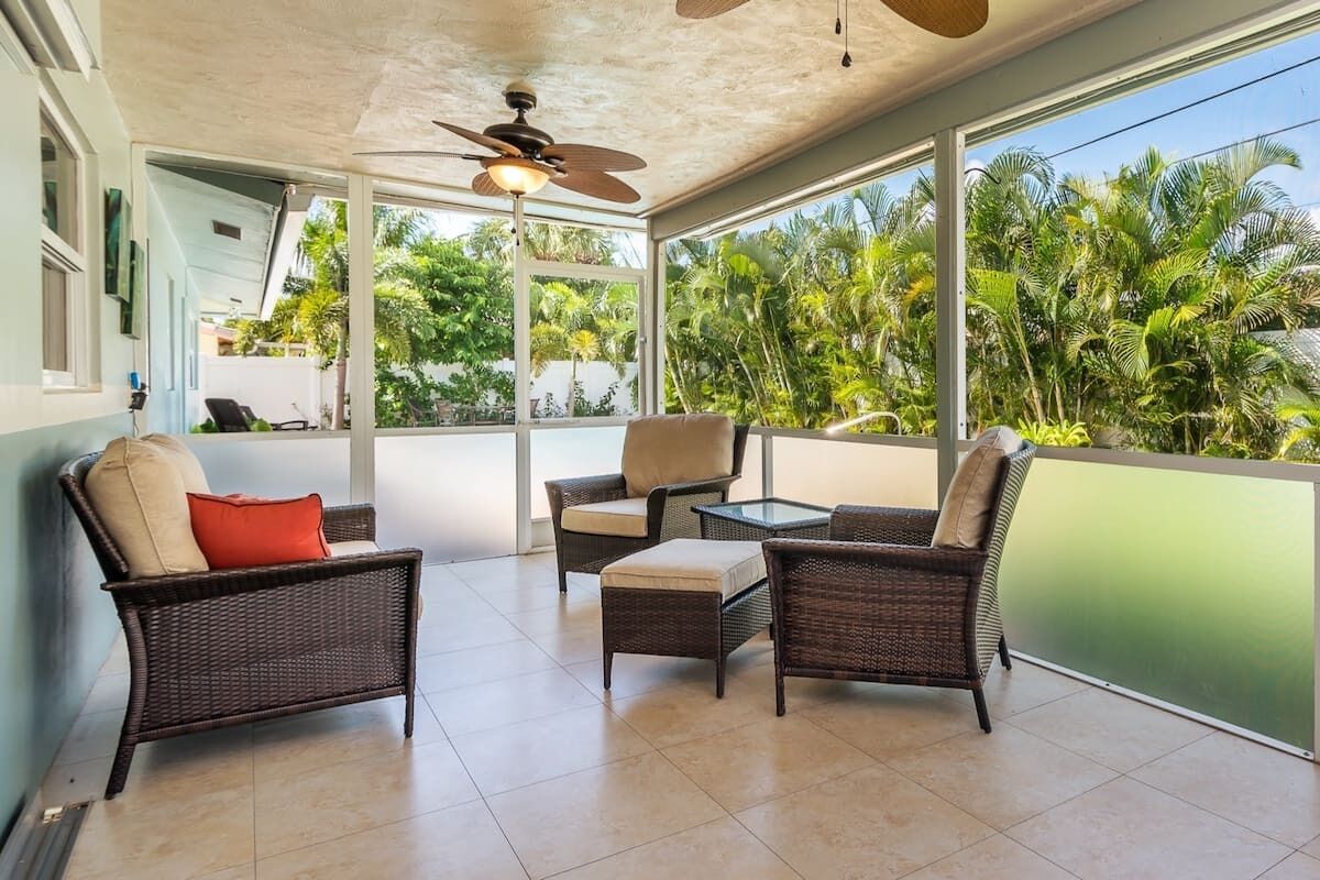 A balcony with wicker furniture, a ceiling fan, and a view of lush greenery.
