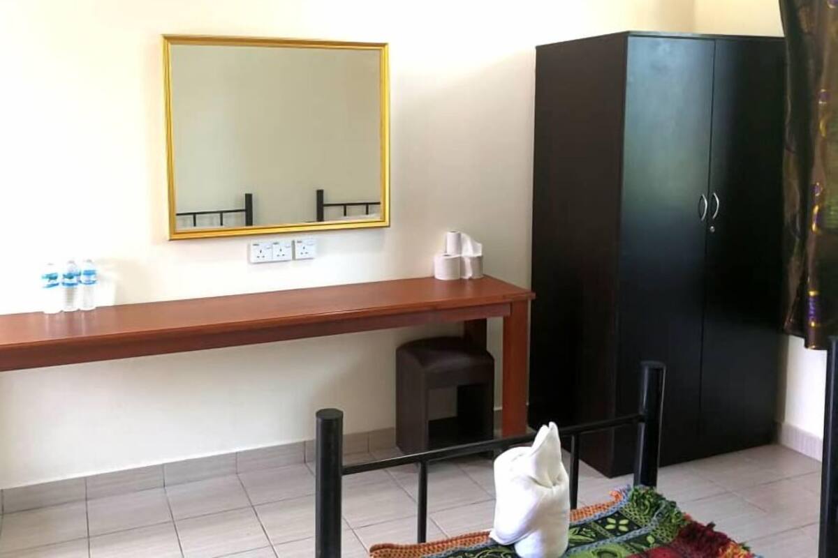 Une pièce avec un bureau en bois, une armoire noire, un miroir et un petit tapis.