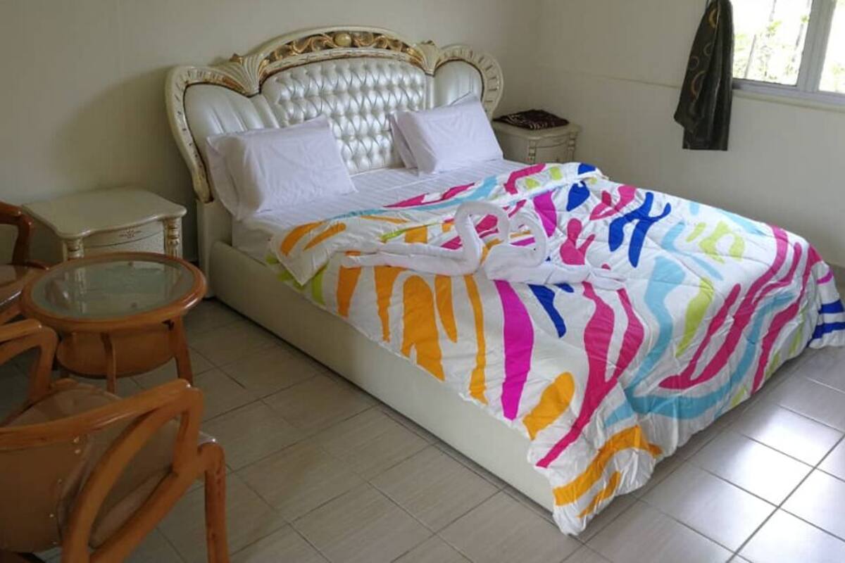 Un lit recouvert d’une couverture aux couleurs vives, une chaise en bois et une petite table.