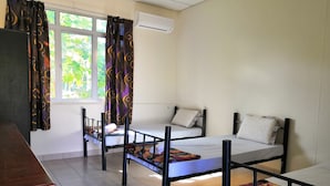 Une chambre de dortoir avec trois lits superposés, un bureau en bois, une fenêtre avec des rideaux et un appareil de climatisation.