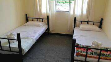 A family room with two single beds, a window with curtains, and a carpeted floor.