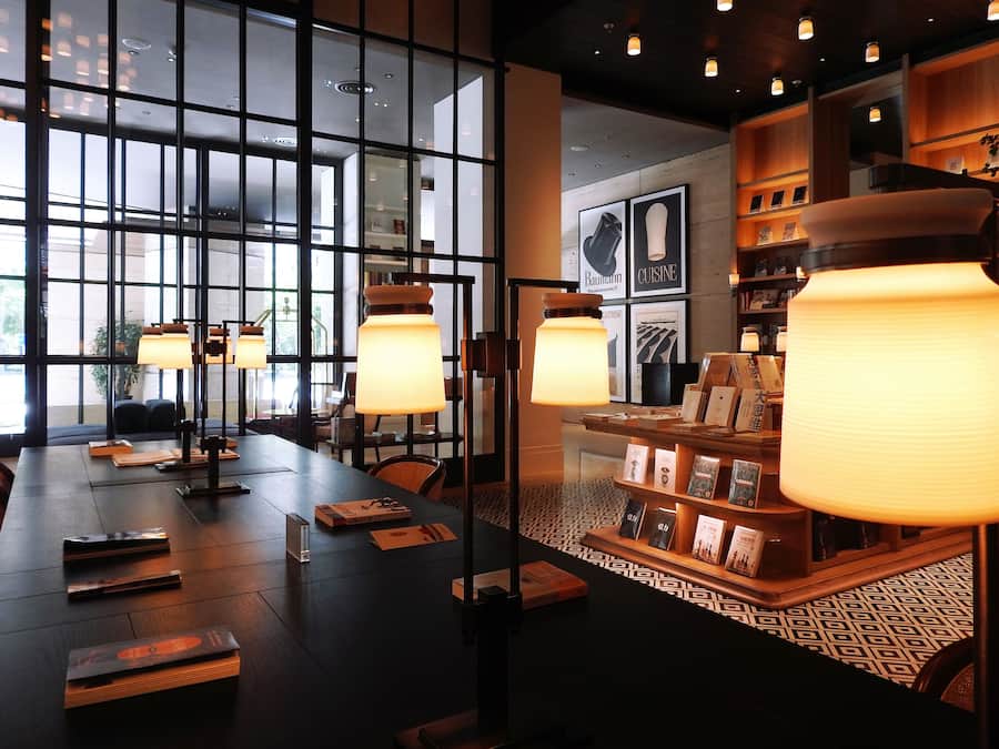 Un interior moderno con una mesa larga, libros y estanterías llenas de libros y objetos decorativos.