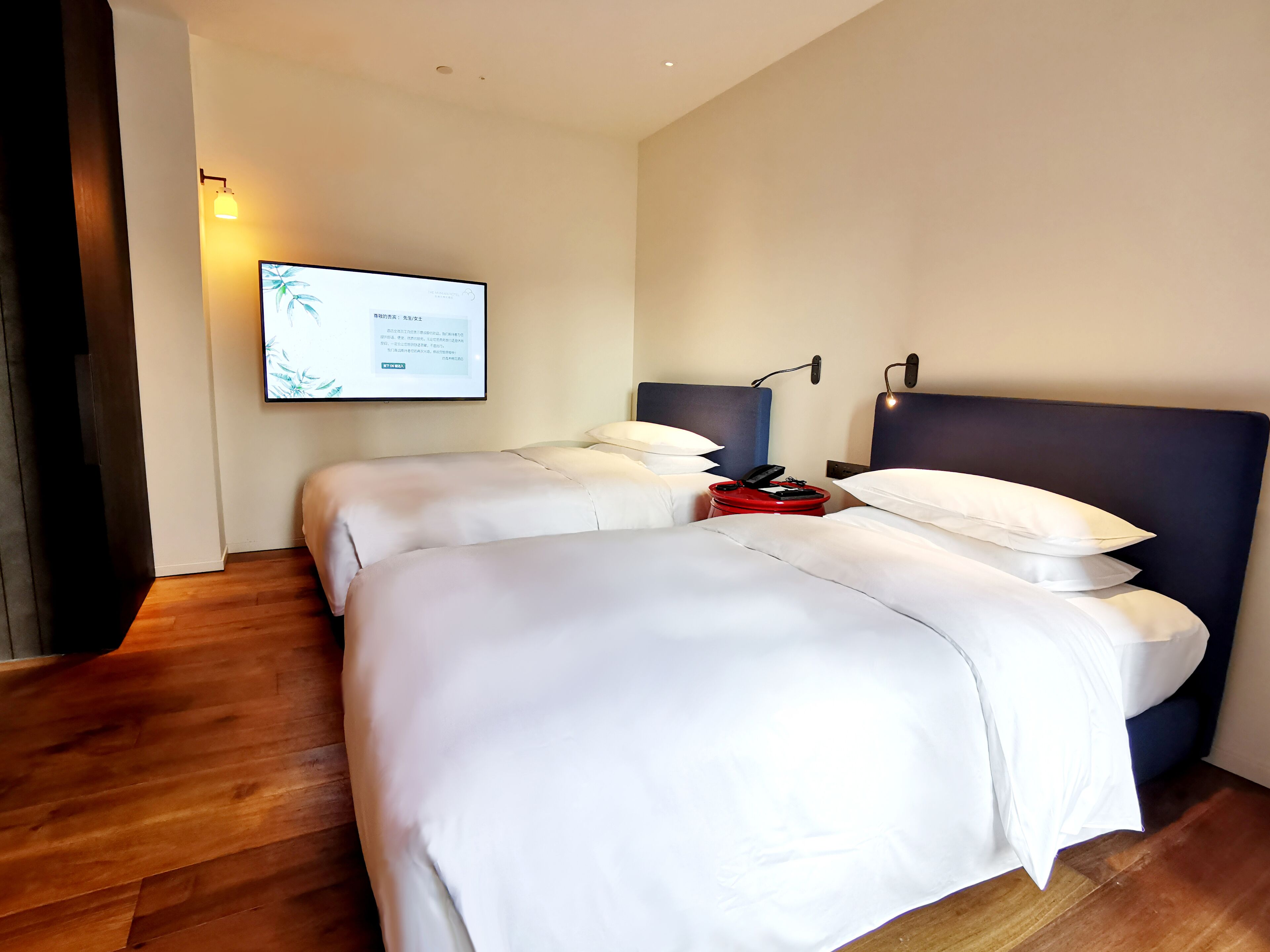 Una habitación de hotel con dos camas, un televisor de pantalla plana montado en la pared y una mesita de noche con un teléfono rojo.