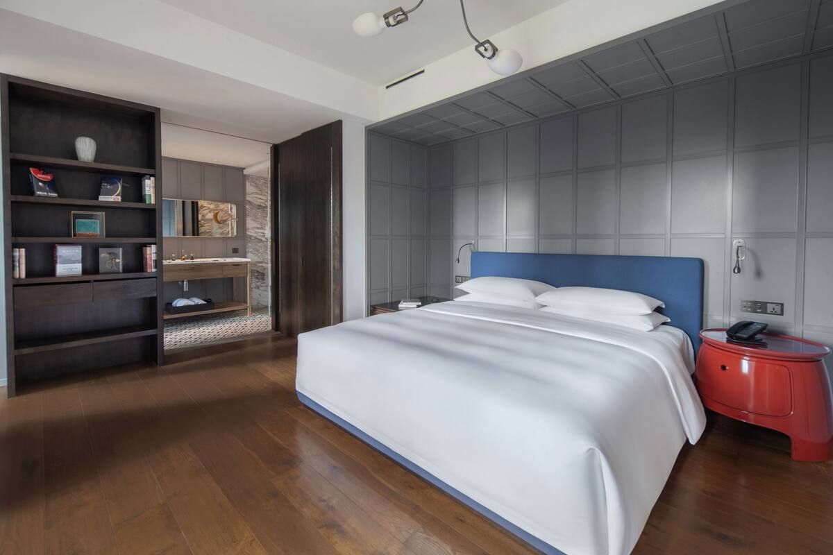 Un dormitorio moderno con una cama grande, suelo de madera, una estantería empotrada y una mesita de noche roja.