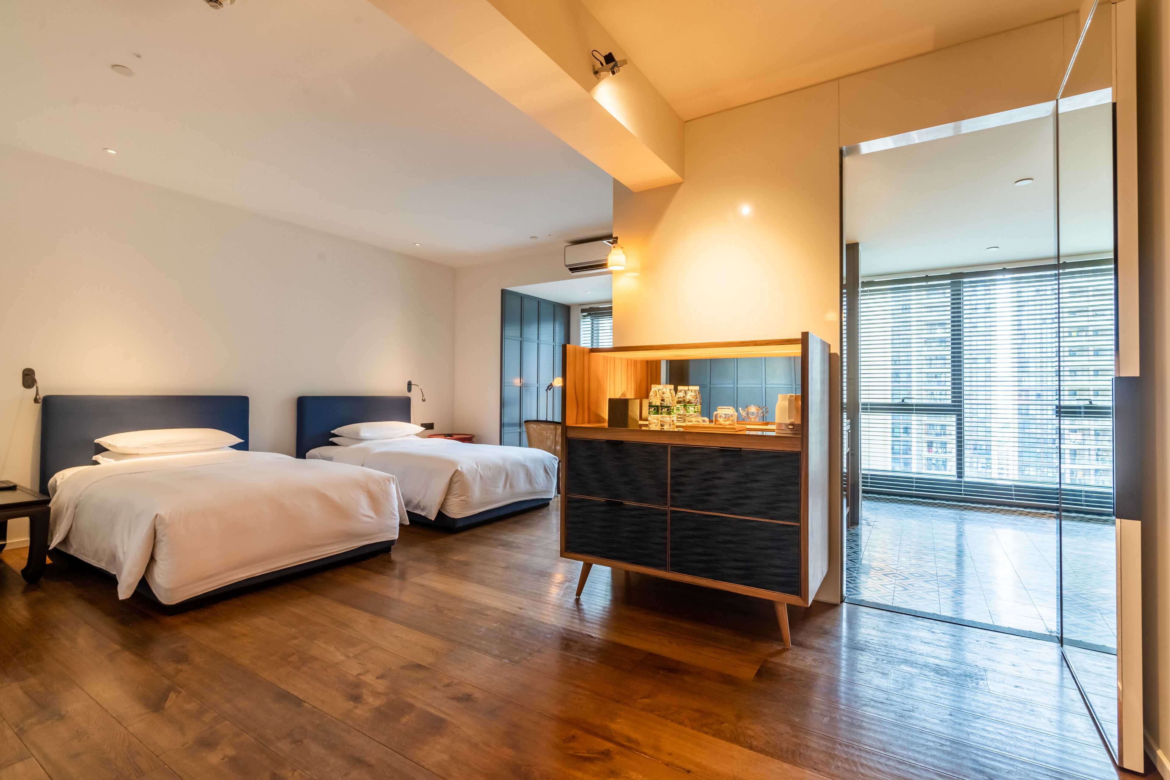 Ein modernes Hotelzimmer mit zwei Betten, einer Holzkombination und einem großen Fenster mit Blick auf die Stadt.