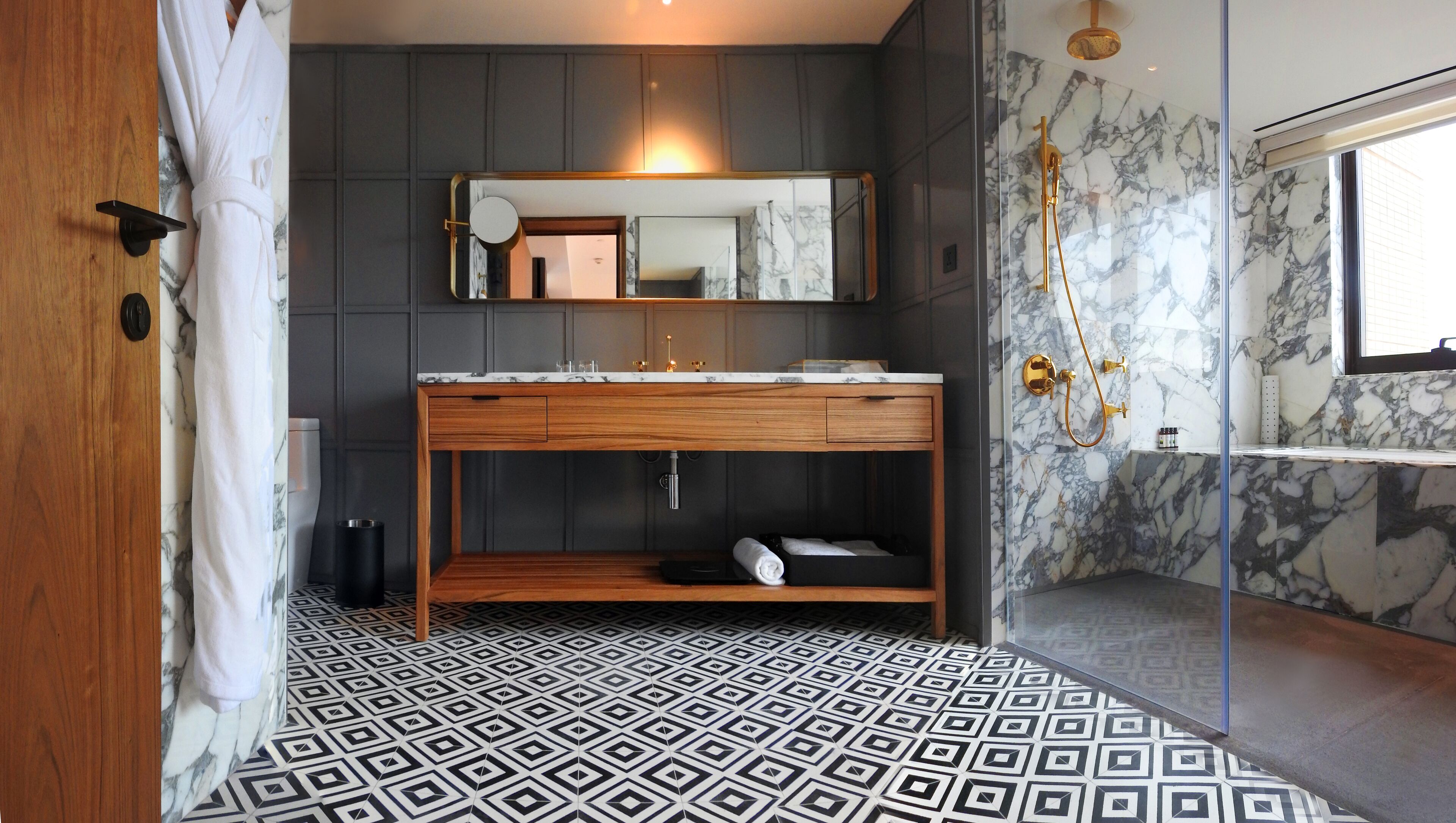 Un baño moderno con ducha de mármol, tocador de madera y piso con diseño geométrico.
