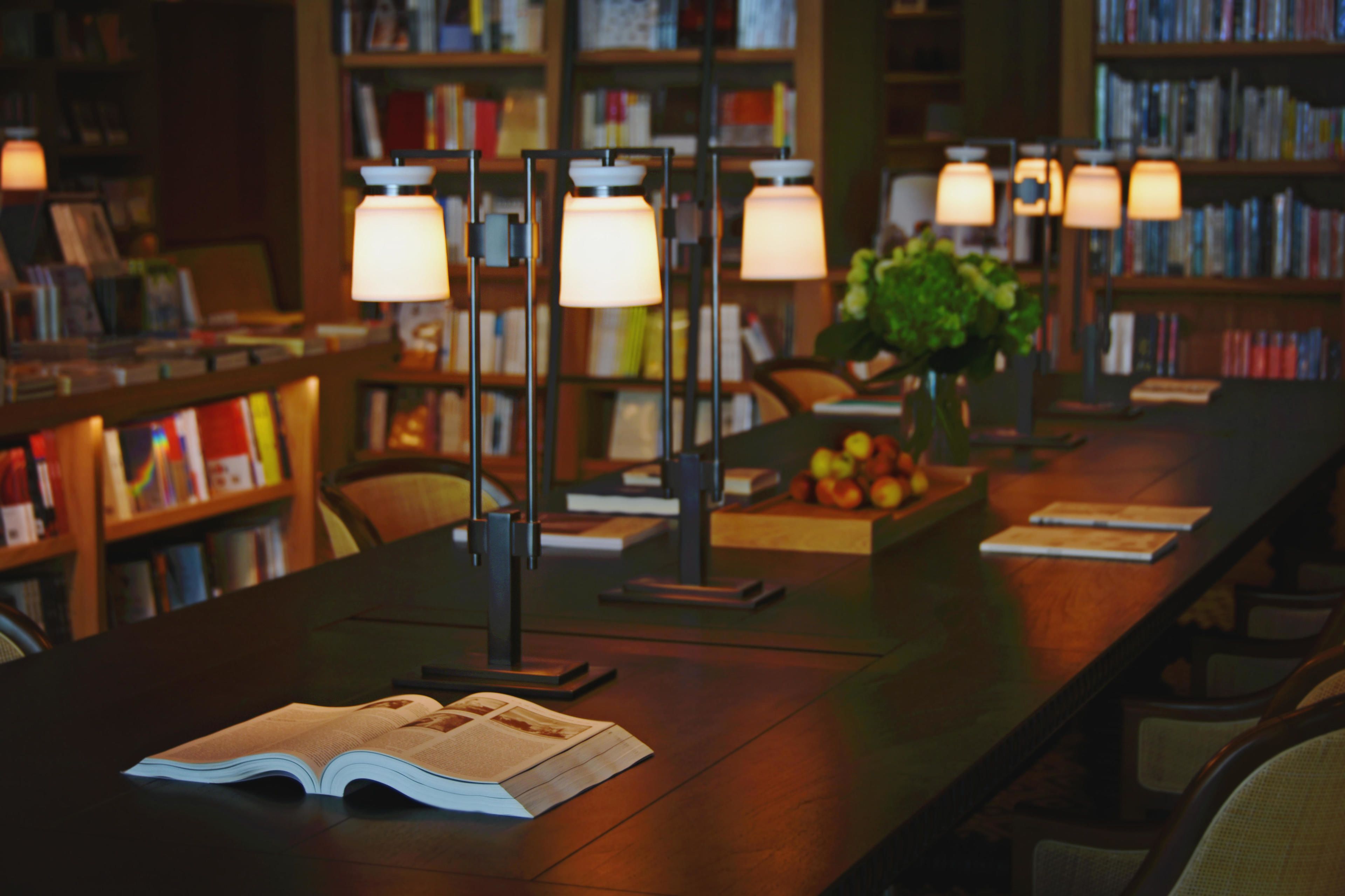 Una biblioteca con estanterías, lámparas de lectura y una mesa con un libro abierto.