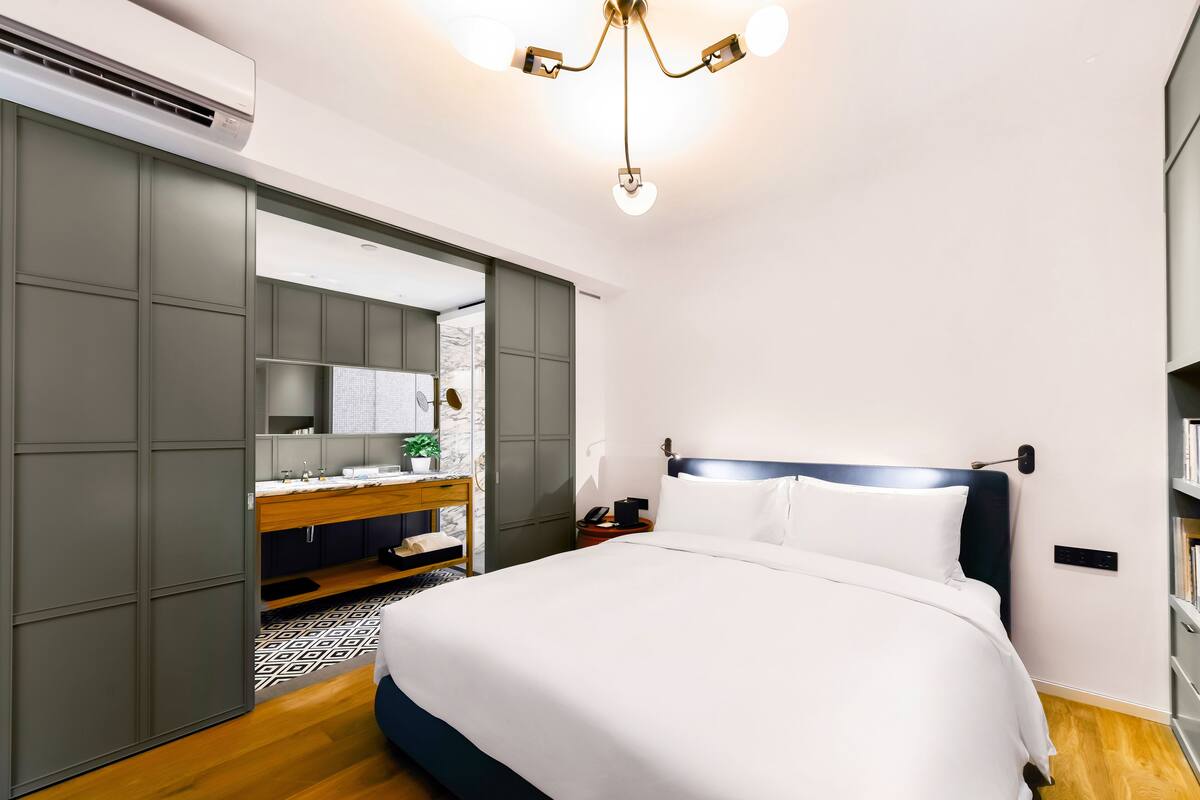 Una habitación de hotel moderna con una cama grande, un armario, una tocador con espejo y una lámpara en el techo.