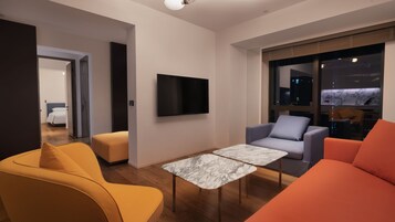 A modern living room with a flat-screen TV, a marble-topped coffee table, and contemporary furniture.