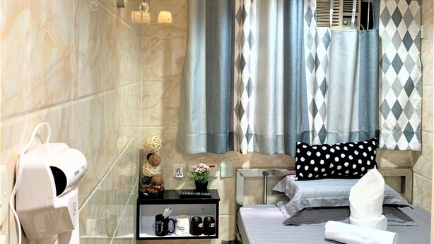 A hotel room with a bed, a vanity with a mirror, a hairdryer, a shelf with toiletries, and a window with curtains. - Super Guest House (Kowloon)