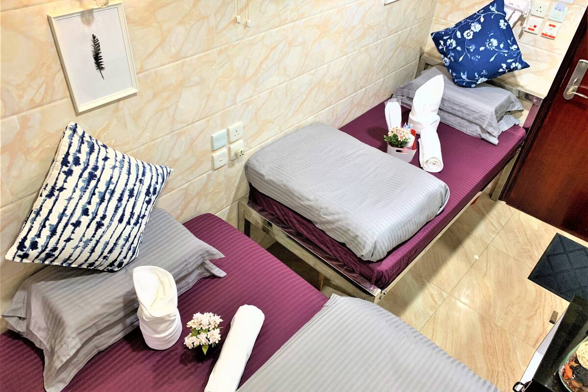 A hotel room with two beds, each with a purple bedspread, white towels, and a blue floral pillow. There is a framed feather on the wall and a small vase with flowers on one bed.
