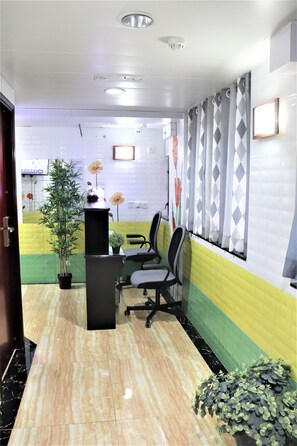 A reception area with a reception desk, chairs, a potted plant, and a wall with patterned curtains. - Super Guest House (Kowloon)