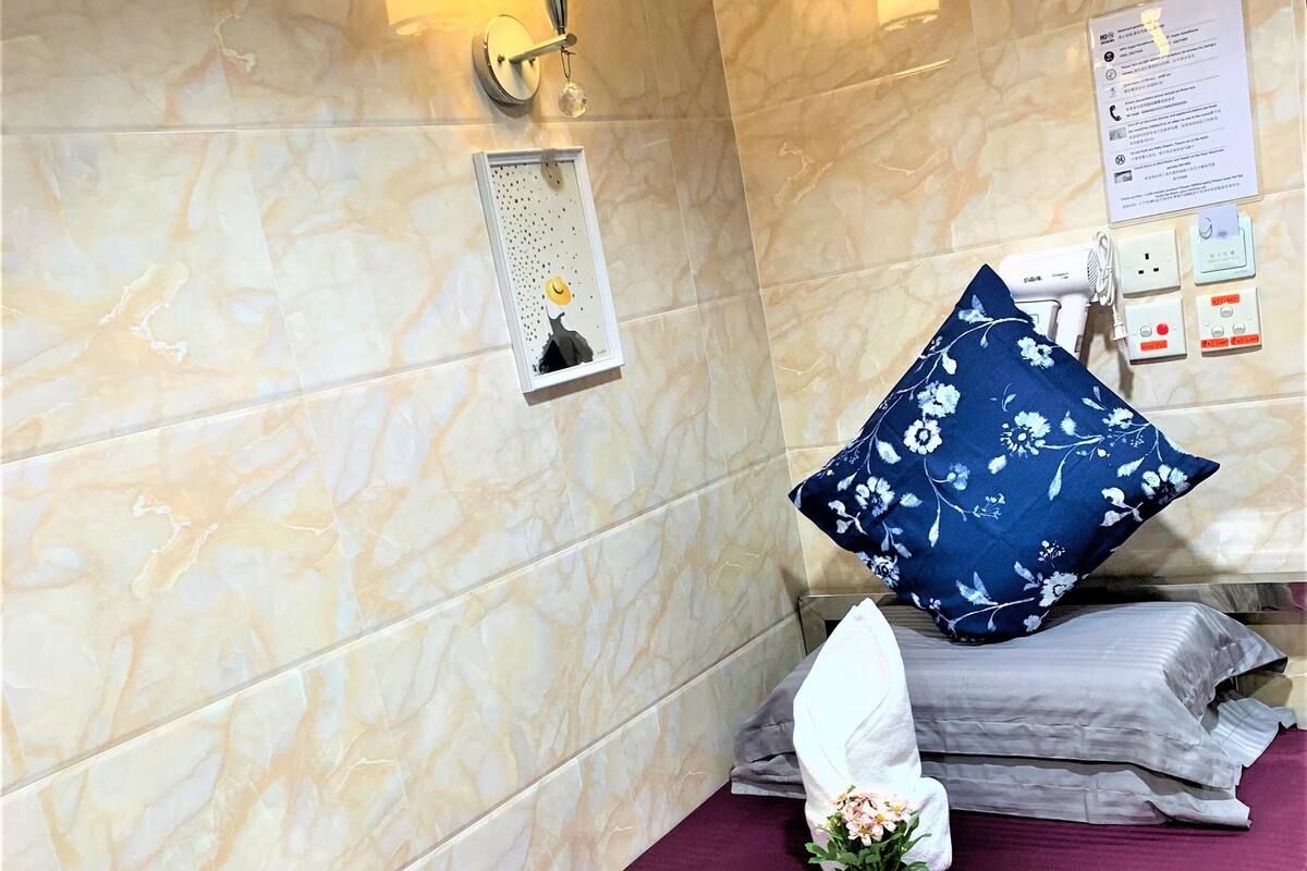 A hotel room with a marble wall, a bed with a purple bedspread, a blue floral pillow, and a wall-mounted lamp.