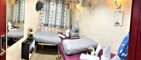 Habitación de hotel con dos camas, baño con ducha, espejo, ventilador e iluminación en la pared.
