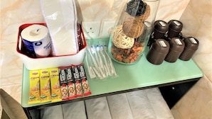 A table with various items including a Nescafe coffee maker, Lipton tea packets, a glass jar with decorative items, and brown containers. - I Top Guest House (Kowloon)
