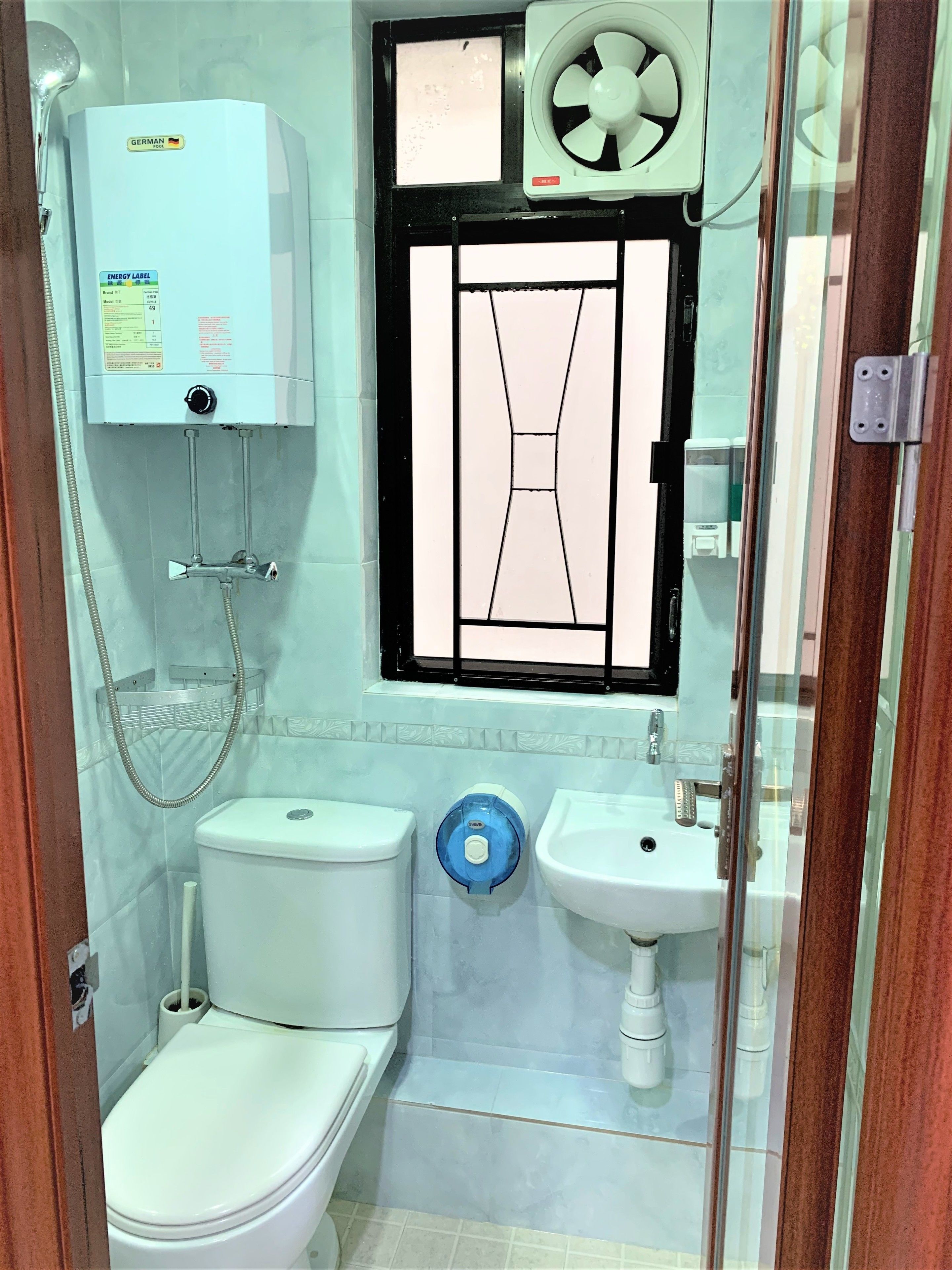 A bathroom with a toilet, sink, shower, and a window with a decorative grille.