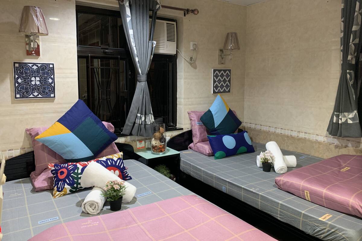 A hotel room with two beds, each with a different patterned bedspread, a window with curtains, wall-mounted lamps, and decorative pillows.