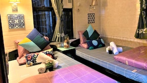 A hotel room with two beds, each with a pillow and a rolled towel. There is a window with curtains, a wall-mounted lamp, and a small table with a plant. - I Top Guest House (Kowloon)
