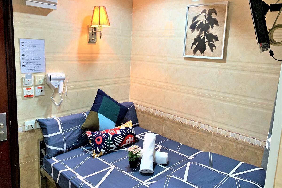 A hotel room with a bed, a wall-mounted lamp, a painting, and a hairdryer.