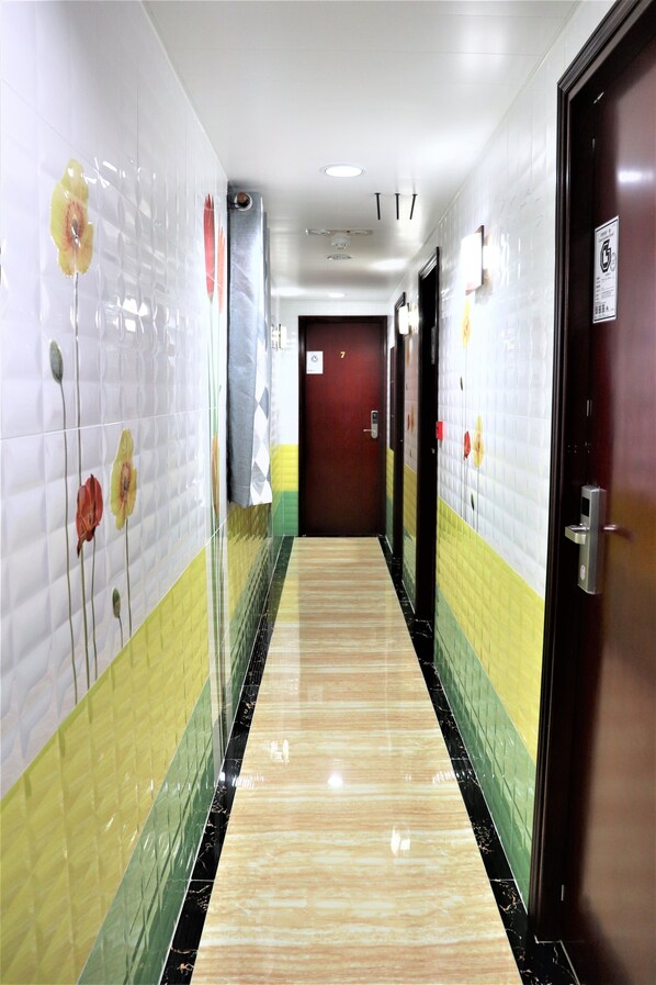 Um corredor com paredes em azulejo, piso de mármore e portas que dão acesso a quartos.