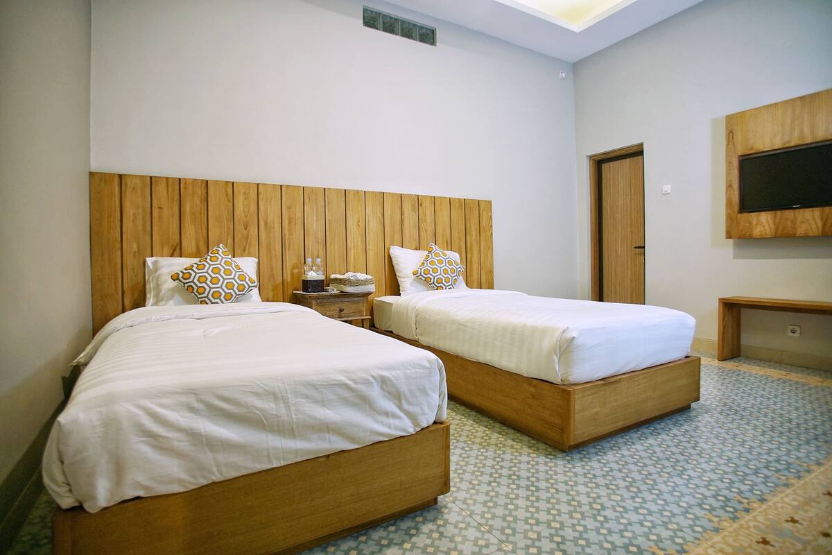 Een hotelkamer met twee houten bedden, een flatscreen-tv aan de muur en een vloer met een patroon.