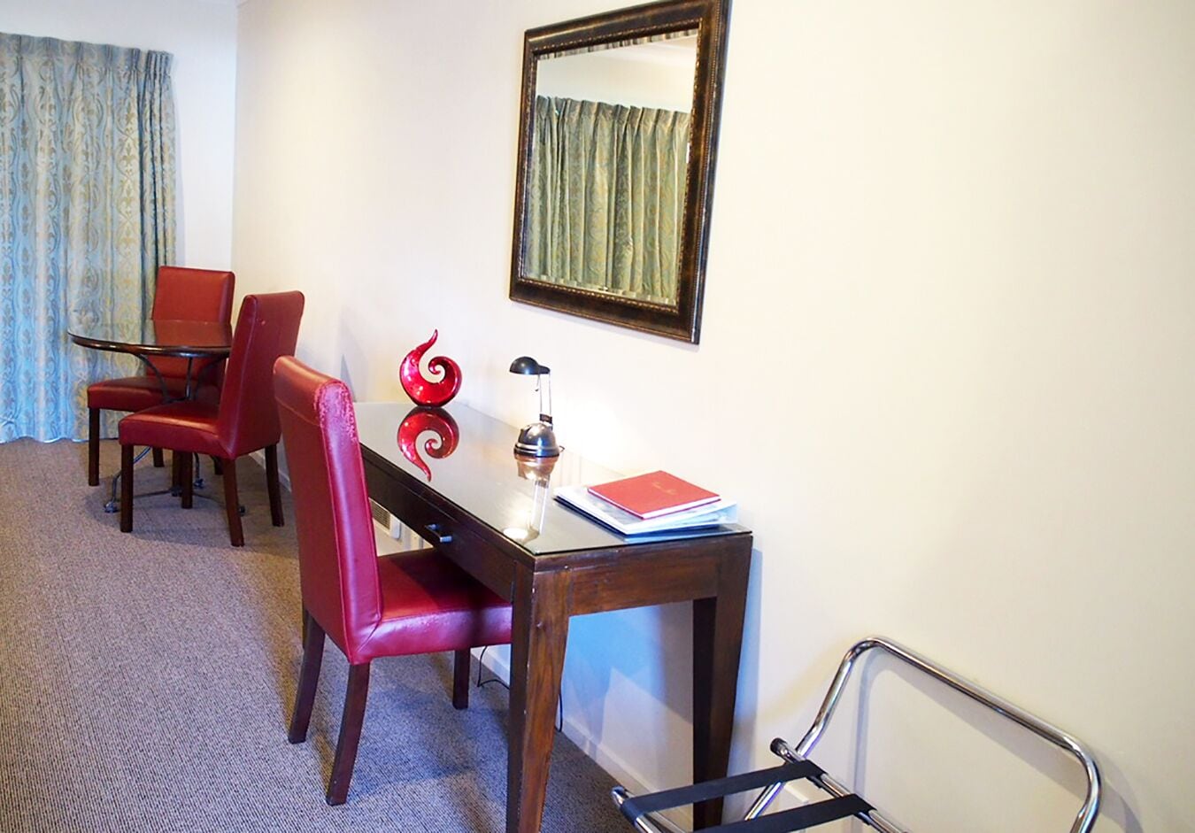 Een hotelkamer met een houten bureau, twee rode stoelen, een spiegel en een rode decoratie.