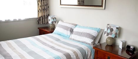 Una cama bien hecha con ropa de cama a rayas, una mesita de noche con lámpara y un espejo en la pared.
