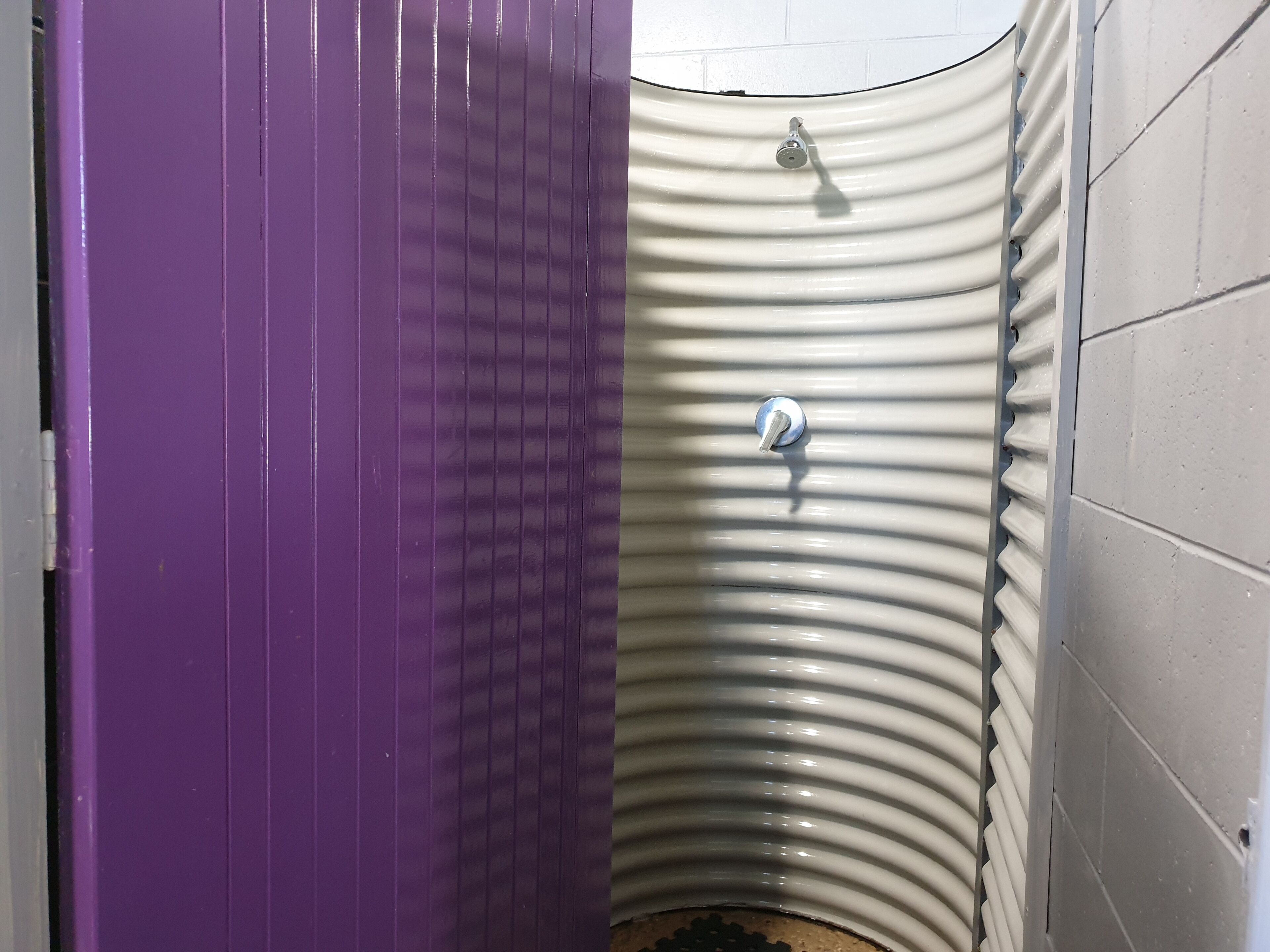 A bathroom with a purple door, a white sink with a curved basin, and a white tiled wall.
