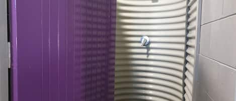 A bathroom with a purple door, a white sink with a curved basin, and a white tiled wall.