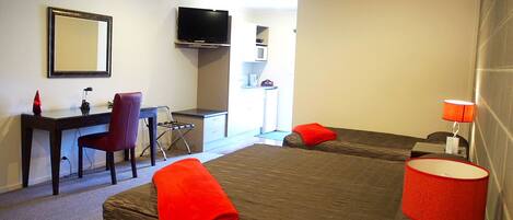 A hotel room with a bed, desk, chair, TV, and a small kitchenette.