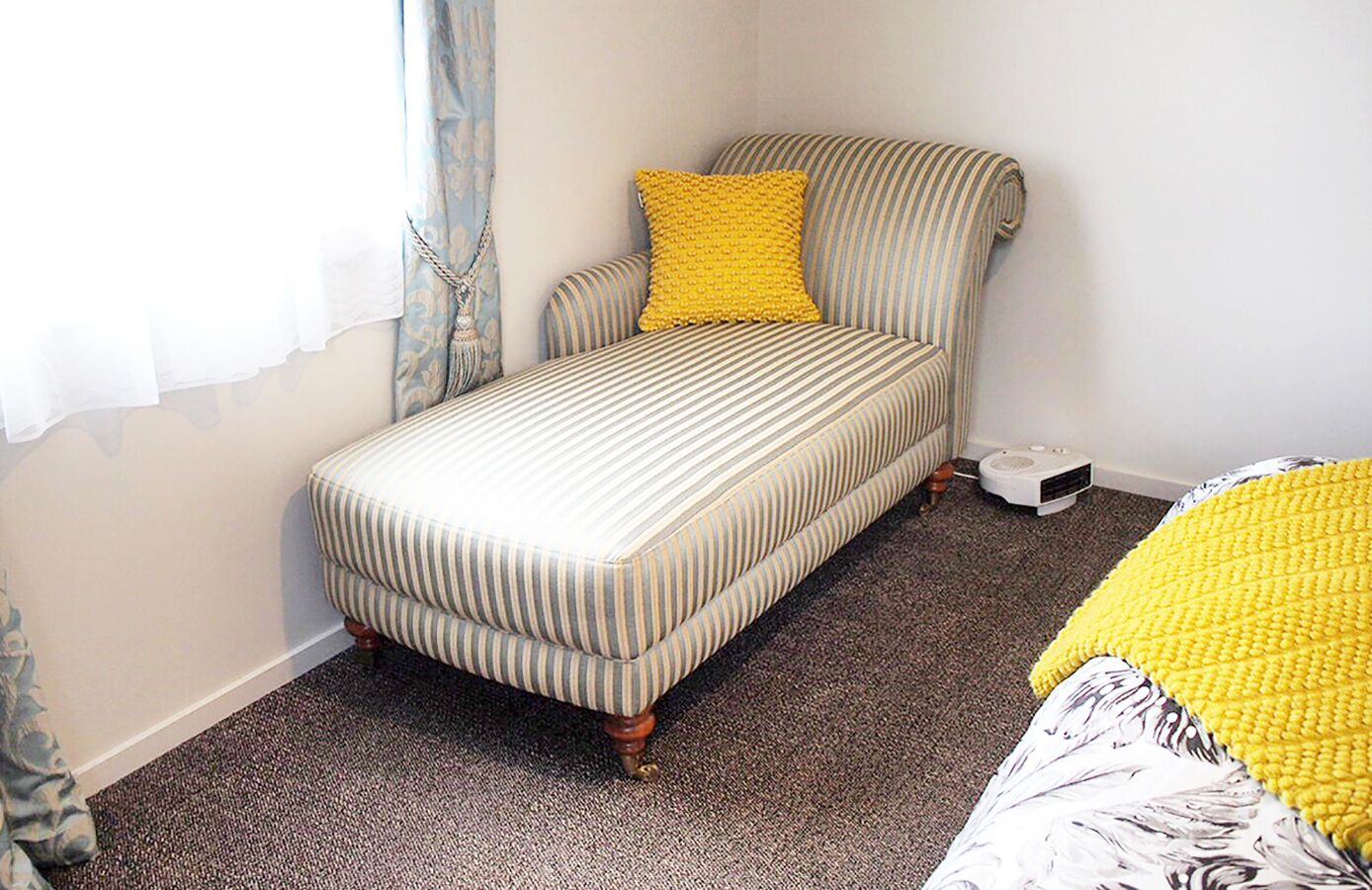 A small, single-bed room with a striped sofa and a yellow pillow.