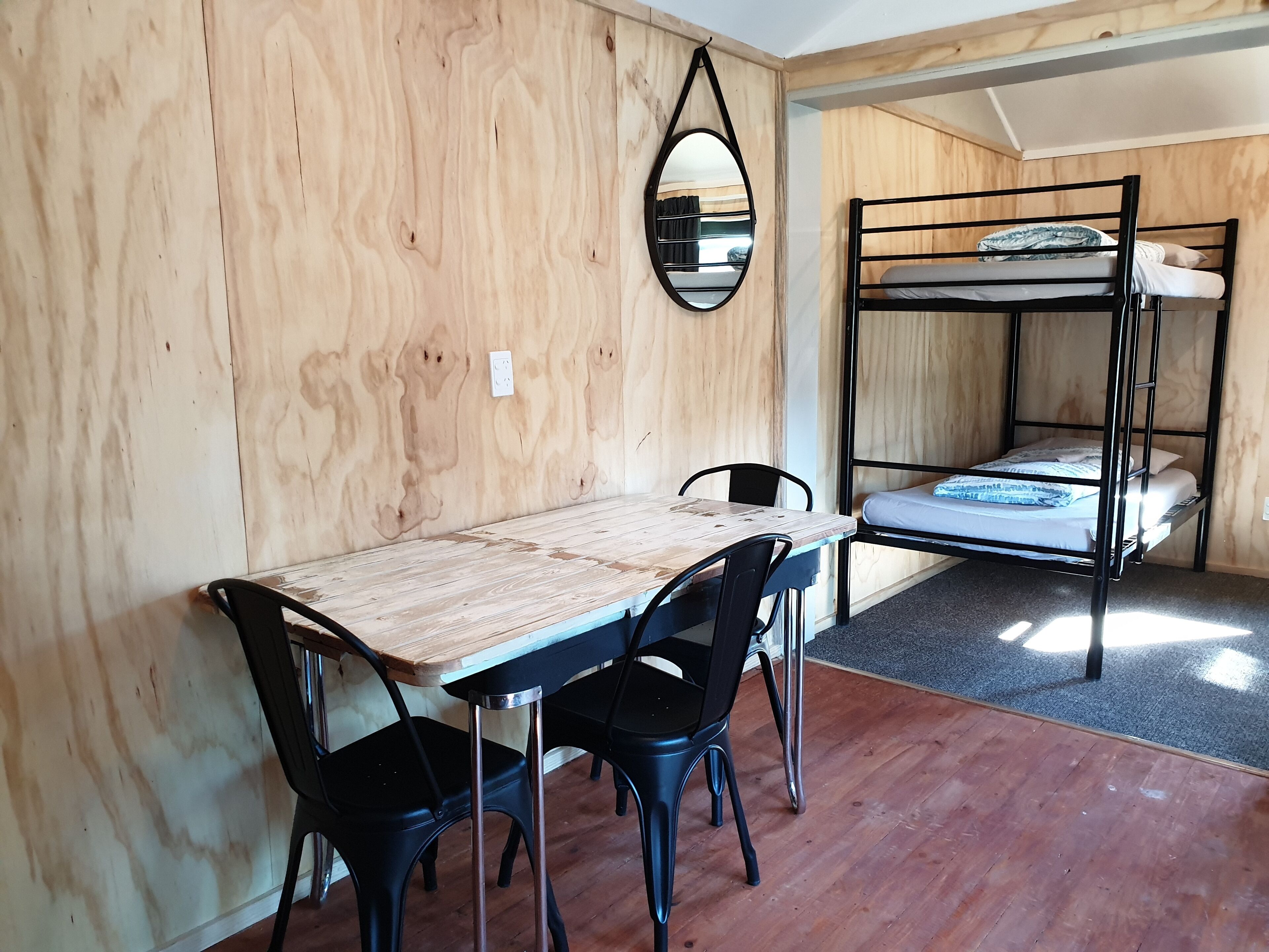 Una habitación con una cama litera de madera, una mesa de comedor con sillas y un espejo colgado.