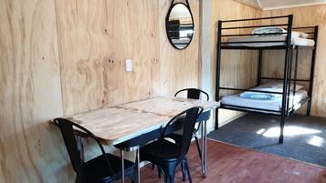 Una habitación con una cama litera de madera, una mesa de comedor con sillas y un espejo colgado.