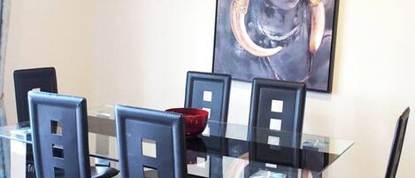A dining area with a glass table and black chairs, a red bowl on the table, and a framed artwork on the wall.