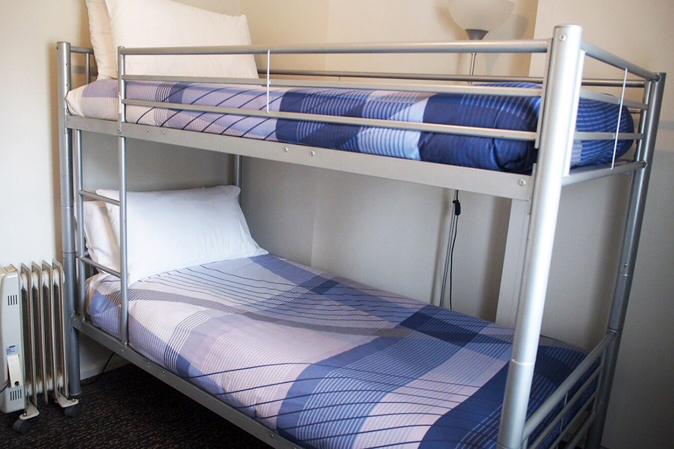 A bunk bed with a checkered bedspread, a white pillow, and a radiator beside it.