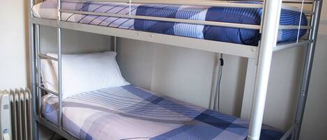 A bunk bed with a checkered bedspread, a white pillow, and a radiator beside it.