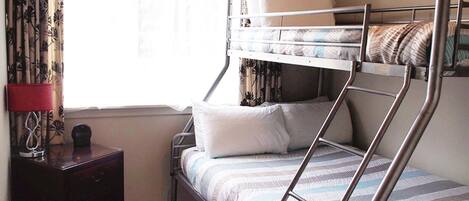 A bunk bed with a striped bedspread, a bedside table with a lamp, and curtains with a floral pattern.