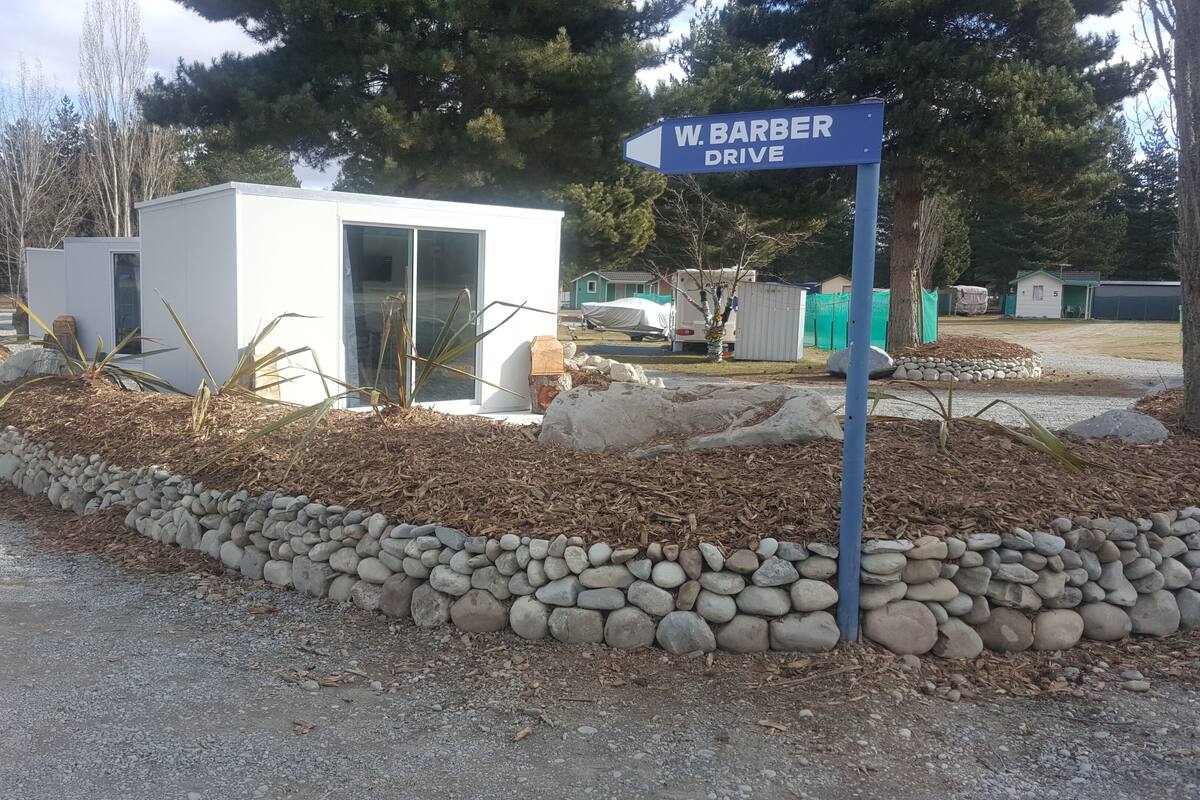 Une zone recouverte de gravier, avec un panneau indiquant « W. Barber Drive�me », bordée d’une murette en pierre et parsemée de quelques plantes.
