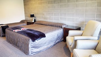 A bedroom with a large bed, a bedside table, a lamp, and a striped armchair.