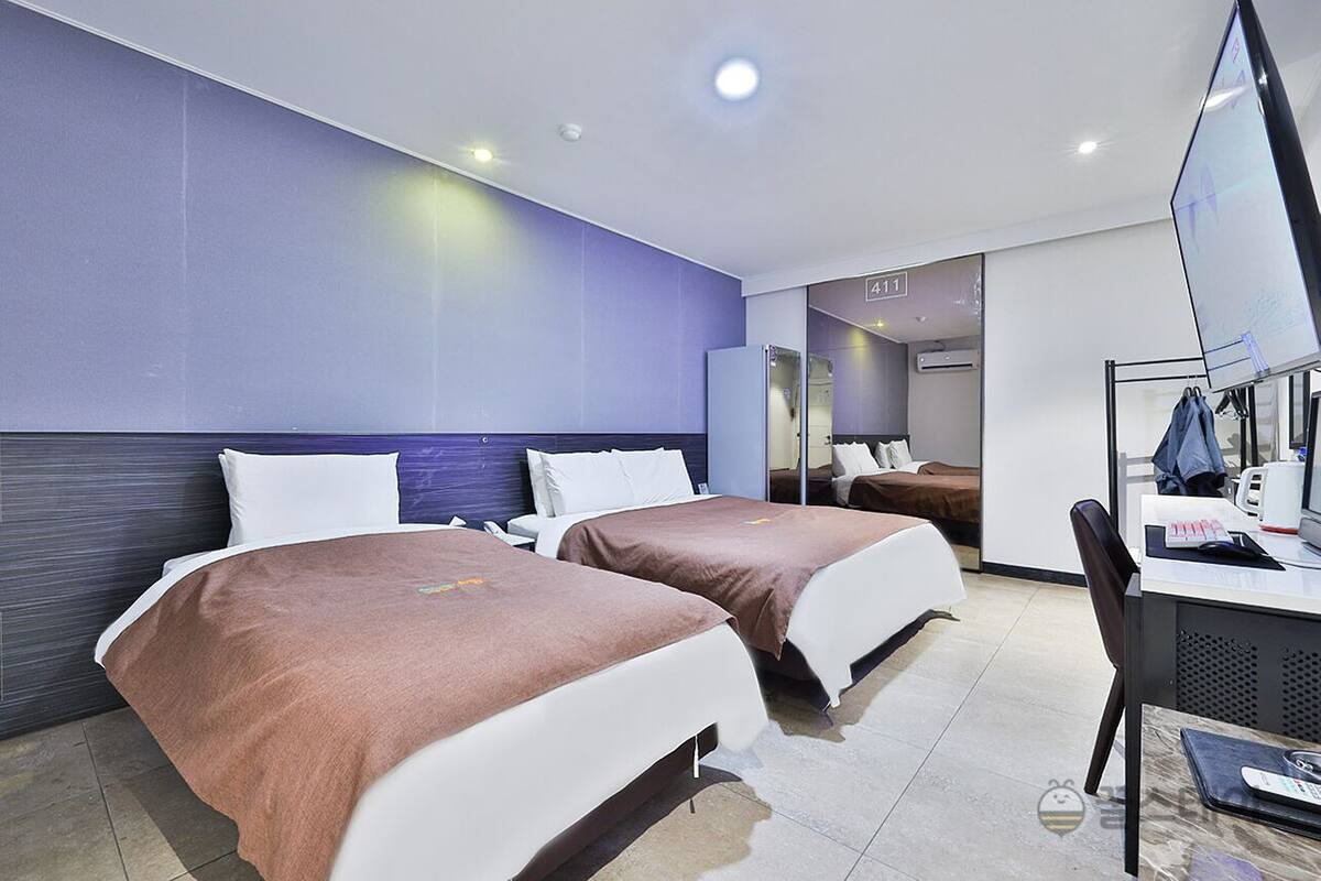 A hotel room with two beds, a desk with a chair, and a large mirror.