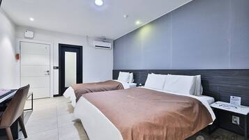 A hotel room with two beds, a desk, and a chair. There is a door, an air conditioning unit, and a nightstand with a lamp.
