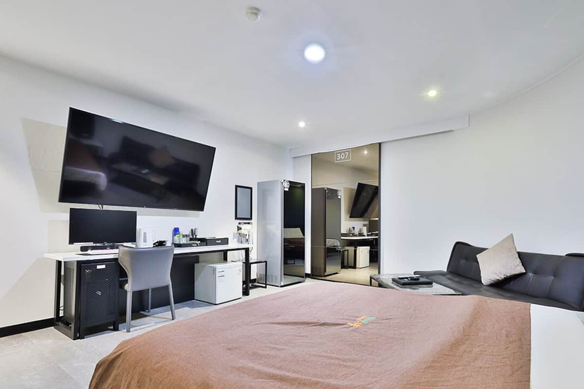 A modern hotel room with a large bed, a desk with a computer, a flat-screen TV, and a seating area with a sofa.