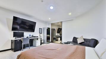 A modern hotel room with a large bed, a desk with a computer, a flat-screen TV, and a seating area with a sofa.