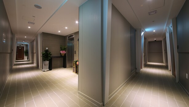 A modern hotel corridor with a tiled floor, recessed lighting, and a potted plant. - Hotel Sopoong (Incheon)