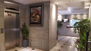 A modern lobby with a digital elevator, a framed artwork, potted plants, and a reception desk labeled "FRONT". - Hotel Sopoong (Incheon)