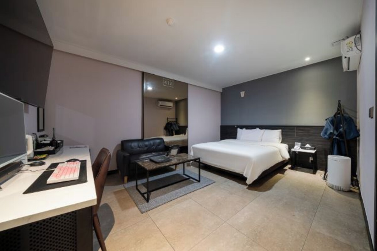 A modern hotel room with a bed, desk, chair, and a small table.