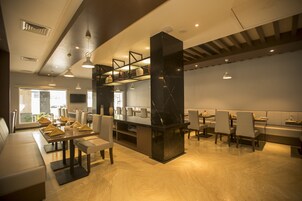 Un restaurante moderno con una columna central de mármol negro, mesas de madera y una zona de estar con bancos acolchados.